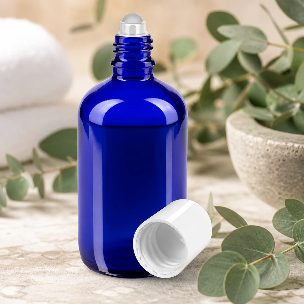 Flacon de pharmacie bleu 100ml Roll-On bouchon blanc Flacon de pharmacie bleu de 100 ml muni d'un applicateur à bille, posé sur un fond de pierre claire à côté de plantes vertes