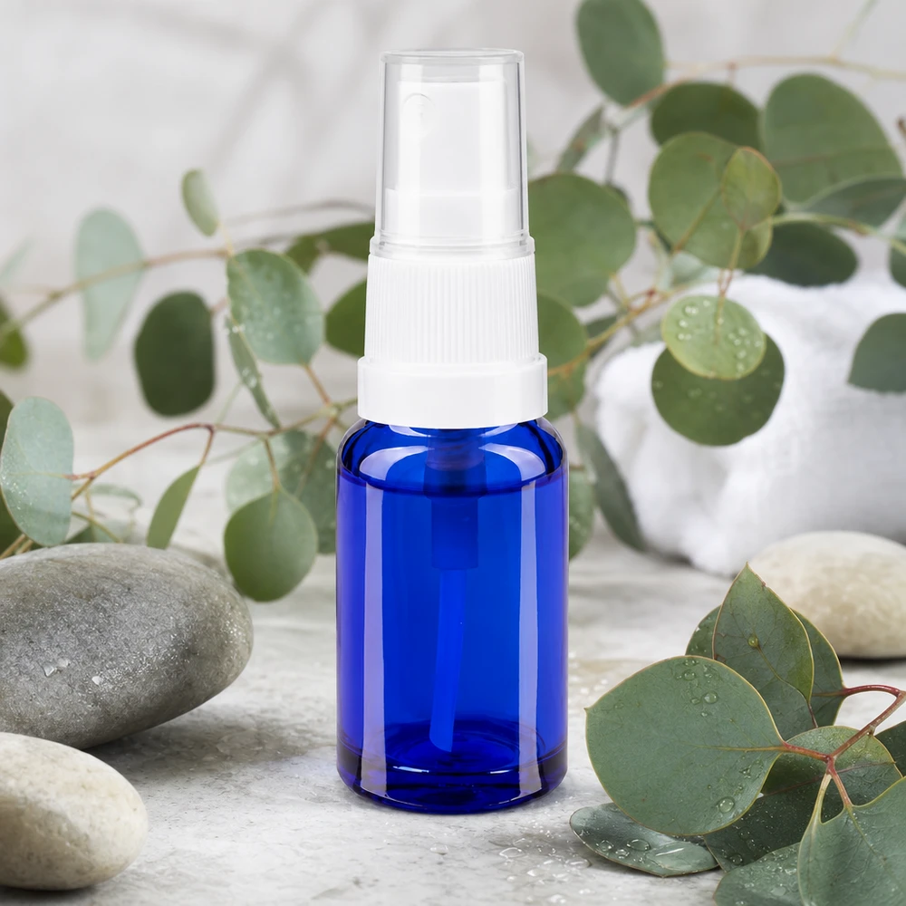 Flacon de pharmacie bleu 10ml embout spray blanc Flacon compact en verre bleu de 10 ml avec pompe standard, posé sur du marbre à côté de pierres de spa