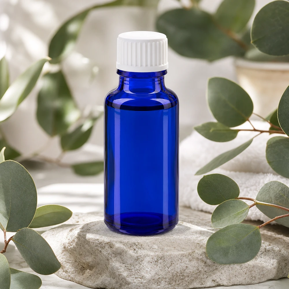 Flacon compte-gouttes bleu cobalt de 20 ml avec bouchon blanc, posé parmi des branches d'eucalyptus