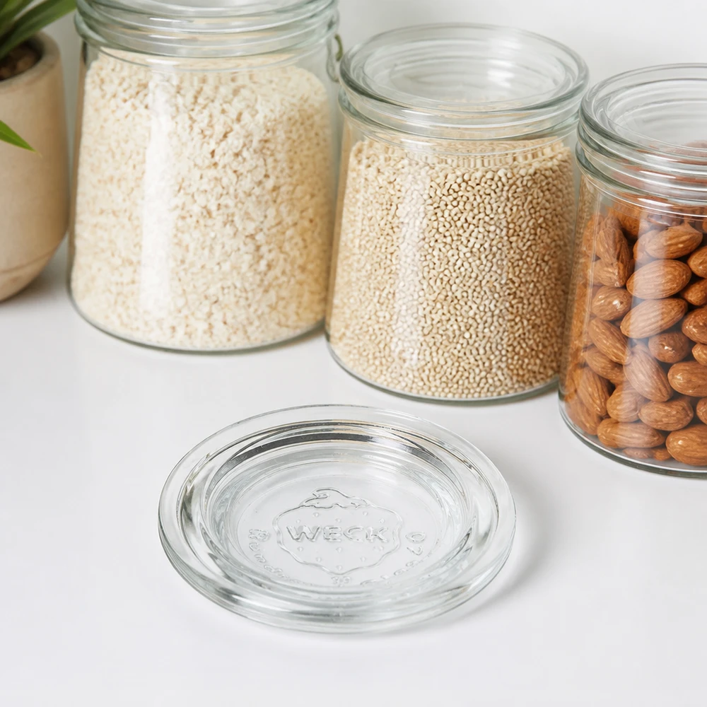 Couvercle en verre WECK RR40 WECK Couvercle en verre RR40 transparent devant des bocaux de stockage avec riz Quinoa et noix sur un plan de travail blanc