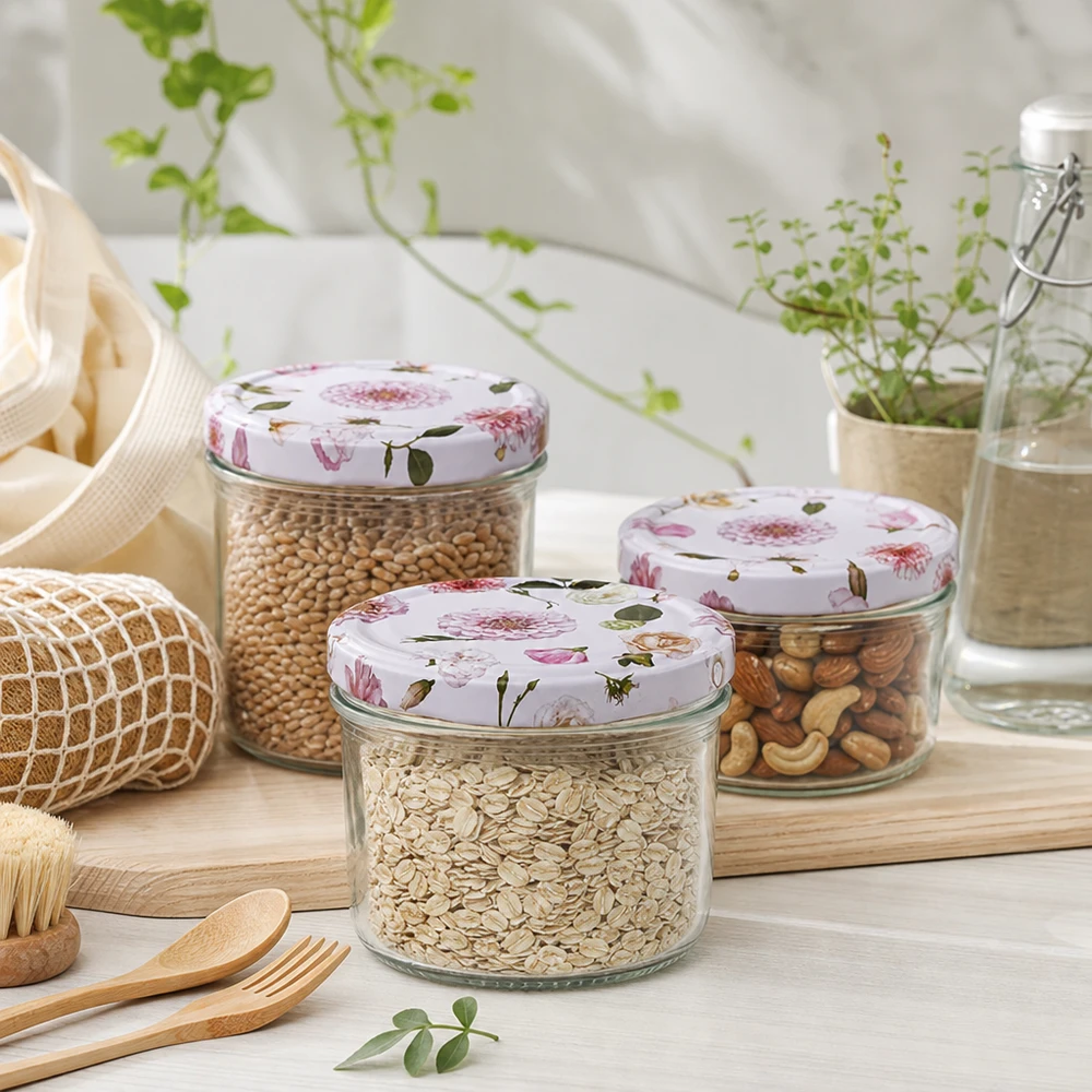 Trois bocaux cylindriques de 230 ml au couvercle rose fleuri remplis de céréales et de noix dans un environnement de cuisine durable