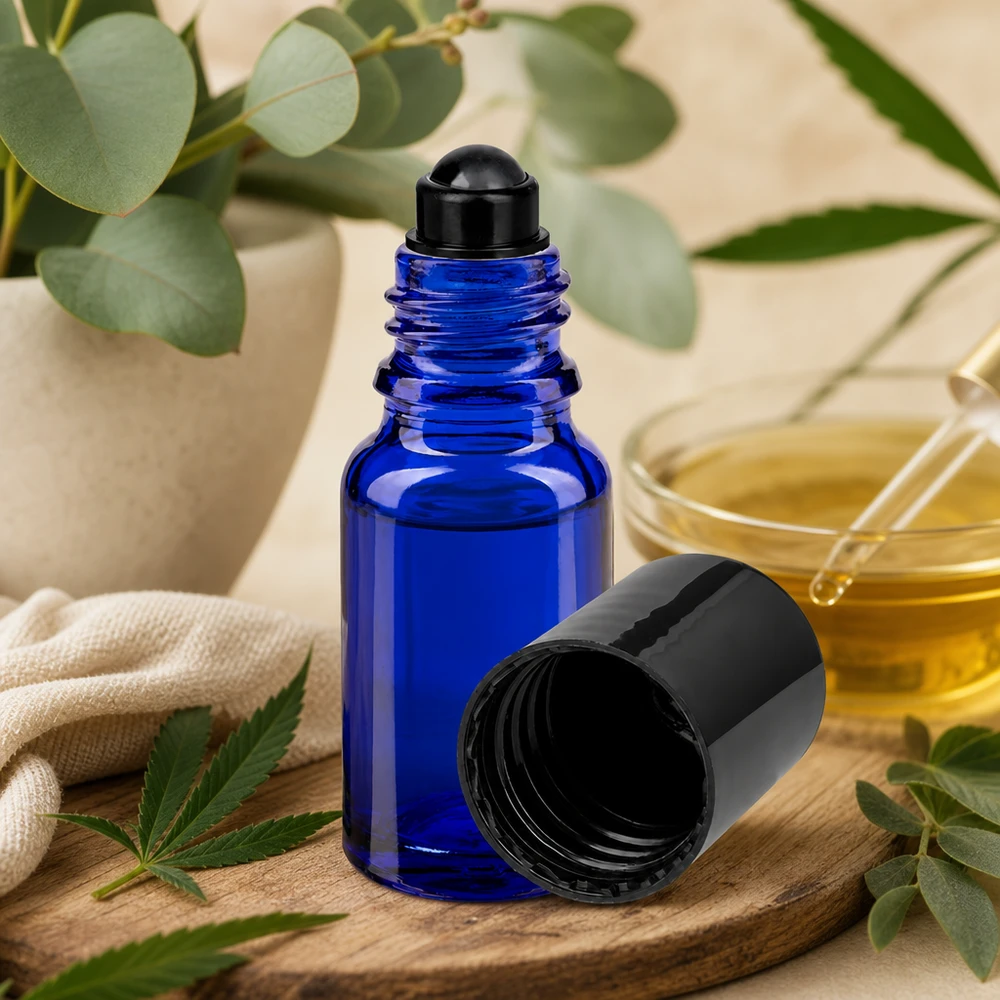 Flacon de déodorant en verre bleu 10 ml, déo à bille vide Flacon roll-on bleu cobalt de 10 ml à côté d'une huile dorée dans un bol en verre et de plantes botaniques