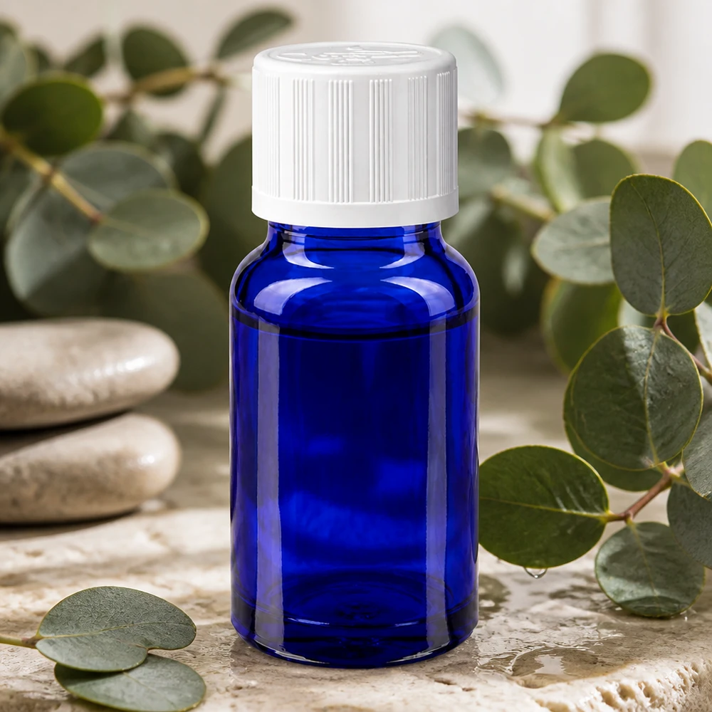 Petite bouteille en verre bleue de 10 ml avec bouchon à pression blanc, posée sur une pierre naturelle ornée de feuilles vertes