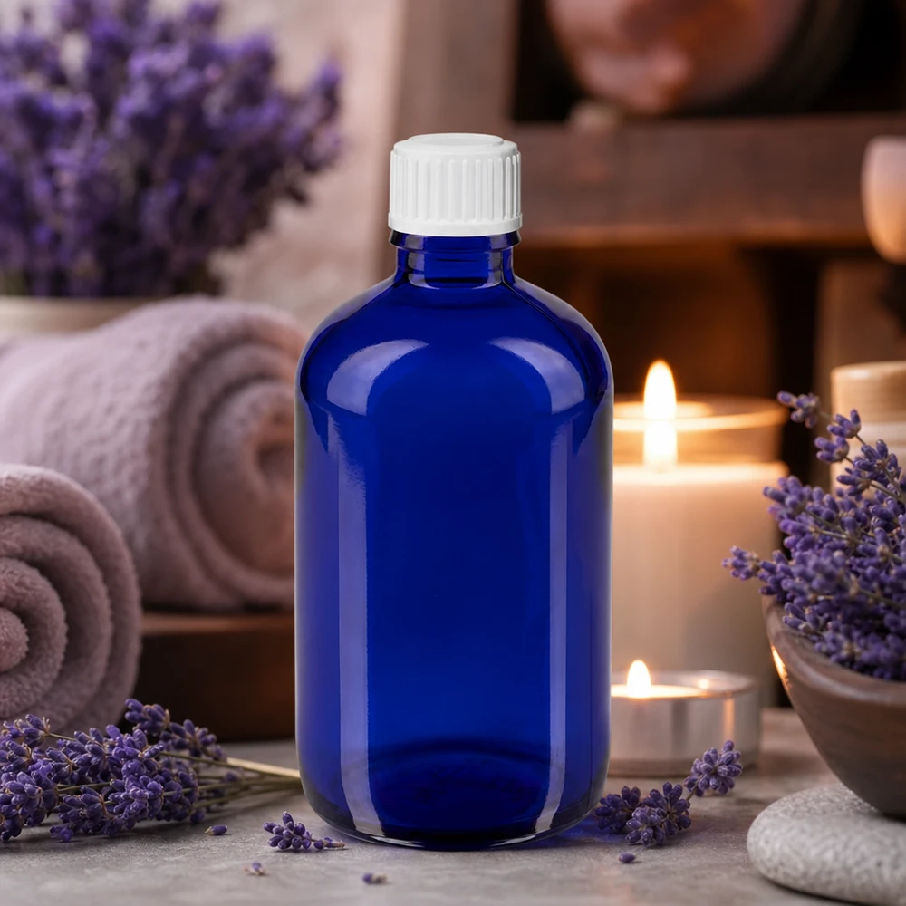 Flacon en verre bleu de 100 ml avec compte-gouttes blanc, entre des fleurs de lavande et des bougies relaxantes