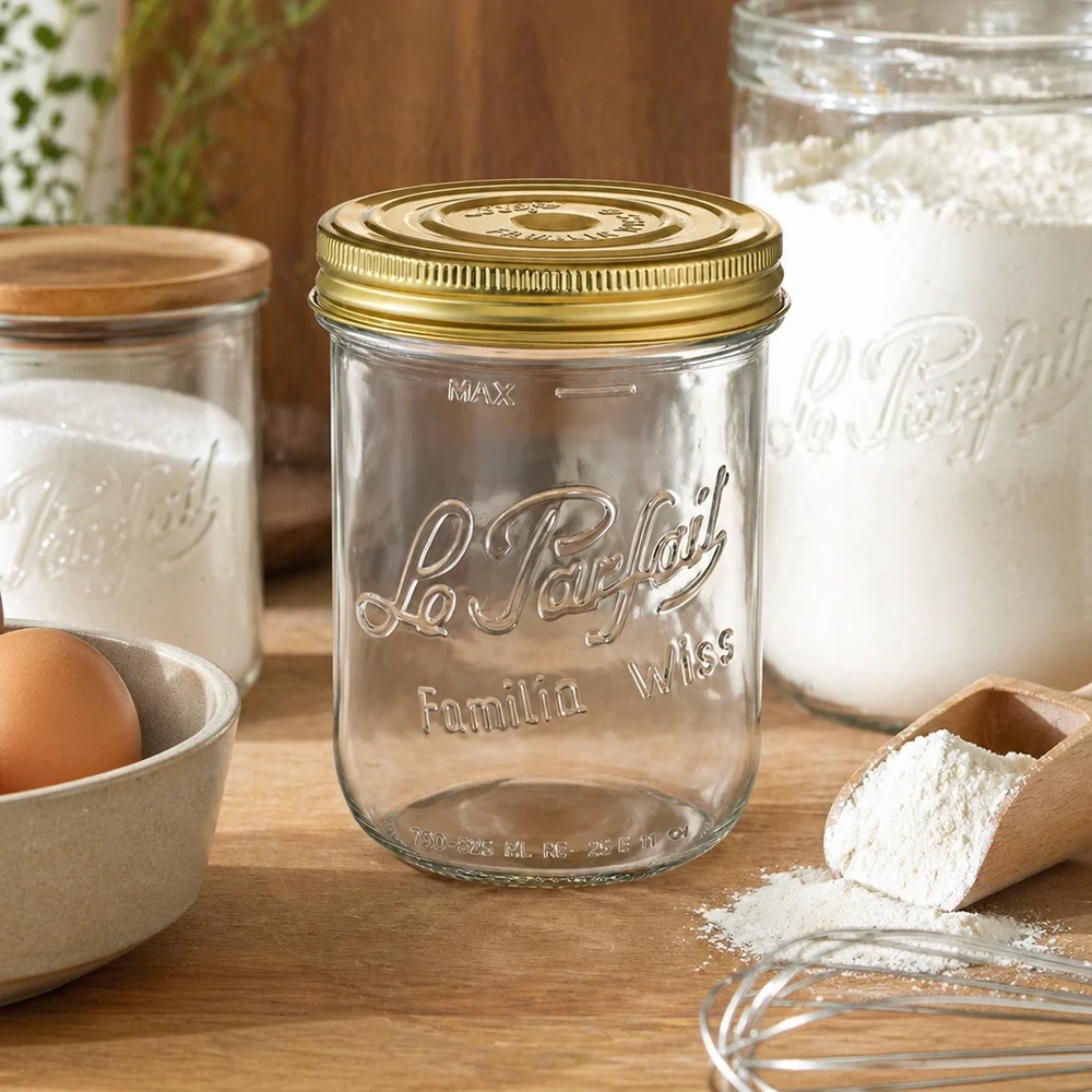 Pot de 1020 ml Familia Wiss avec couvercle doré sur une table en bois à côté d'ingrédients de pâtisserie et d'autres bocaux.