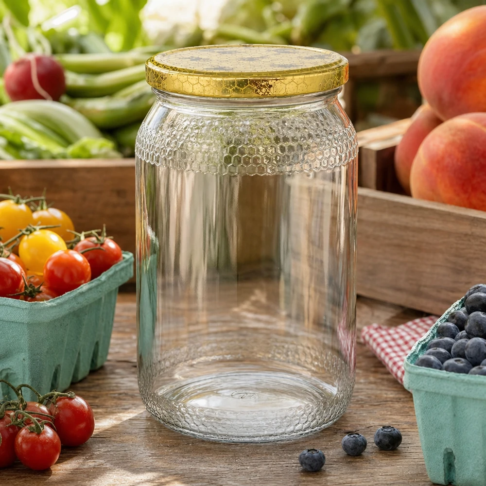 Pot de miel de 900ml vide avec couvercle doré en nid d'abeille entre des fruits et légumes frais sur une table de cuisine en bois