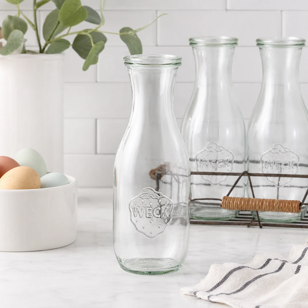 WECK Bouteille de jus de fruit 1062ml Bouteille en verre vide dans une cuisine blanche moderne avec coquille d'oeuf panier en fil métallique et plante