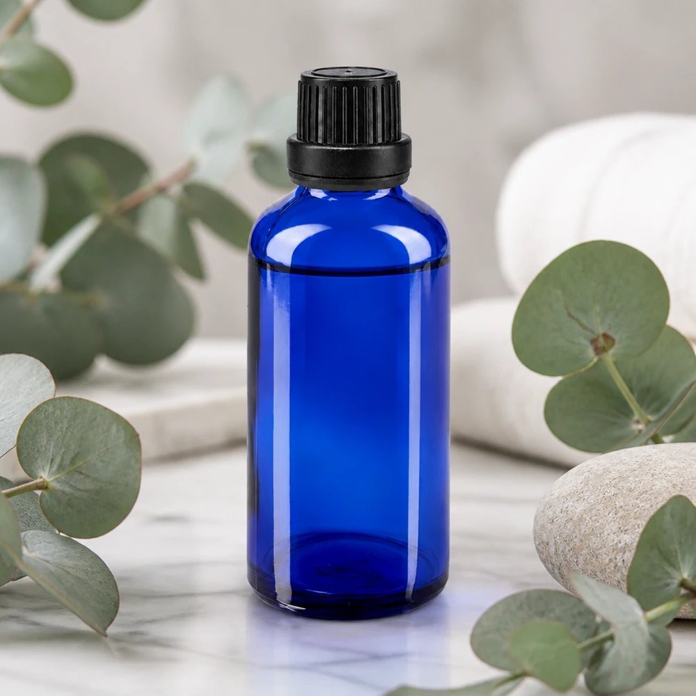 Flacon en verre bleu de 50 ml muni d'un compte-gouttes de 2 mm, posé sur un socle en marbre agrémenté de pierres naturelles et de plantes vertes