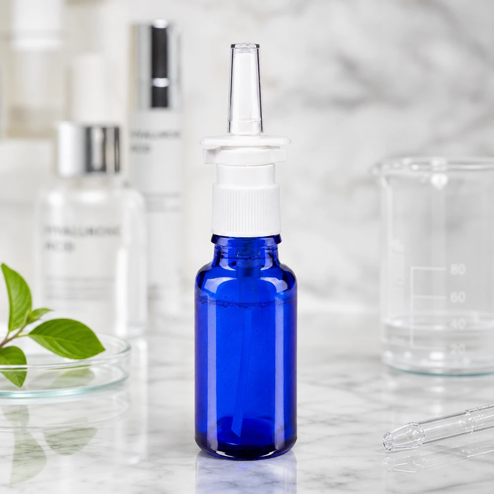 Flacon en verre bleu cobalt de 20 ml muni d'une pompe pour spray nasal et d'une buse d'application transparente, dans un environnement de laboratoire