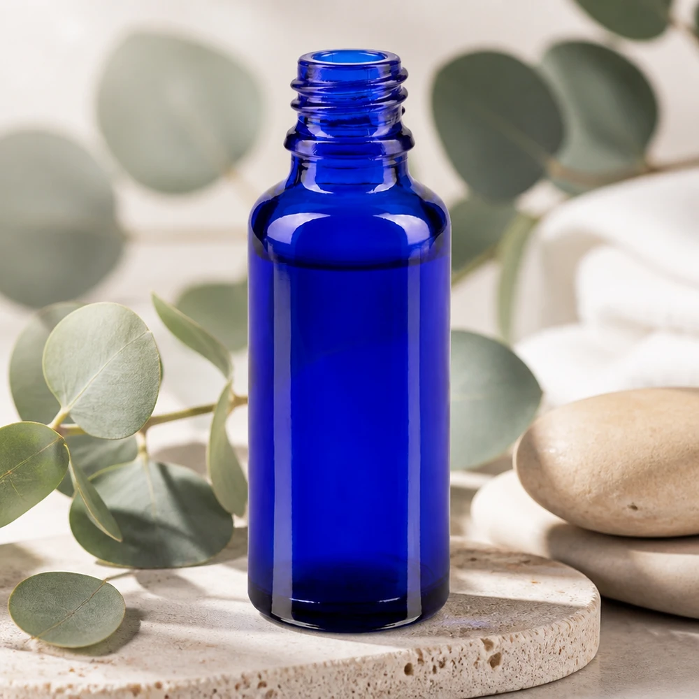 Flacon compte-gouttes pour pharmacie 30 ml DIN18 - verre bleu Petite bouteille en verre bleu ApoGlas de 30 ml posée sur une pierre naturelle, agrémentée de brindilles d'eucalyptus, dans un style bien-être