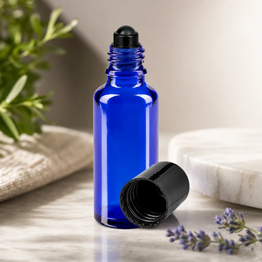 Flacon de déodorant en verre bleu 30 ml, déo à bille vide Flacon roll-on ApoGlas bleu de 30 ml avec applicateur à bille, posé sur du marbre et orné d'herbes naturelles