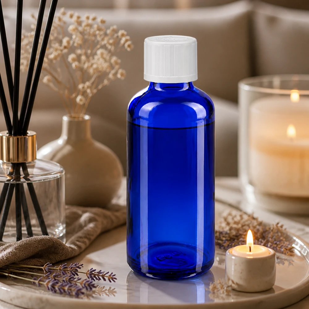 Flacon en verre bleu de 50 ml muni d'un compte-gouttes de 1,2 mm, à côté d'un diffuseur de parfum d'ambiance et d'une bougie chauffe-plat posés sur un plateau en marbre