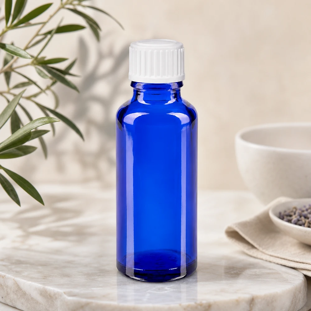Flacon de pharmacie bleu de 30 ml posé sur un socle en marbre, à côté de brins de lavande et d'eucalyptus