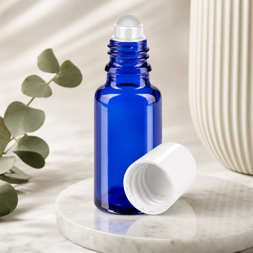 Flacon en verre bleu cobalt avec une bille roulante transparente et un bouchon blanc, à côté d'une branche d'eucalyptus