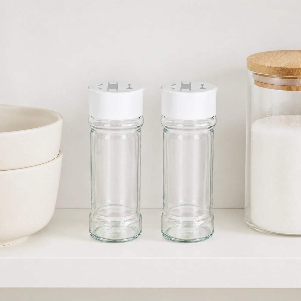 Pot à sel/épices 100 ml avec double saupoudreuse, blanc Deux bocaux à épices de 100 ml, munis d'un couvercle blanc à double saupoudreuse, placés côte à côte sur une étagère blanche