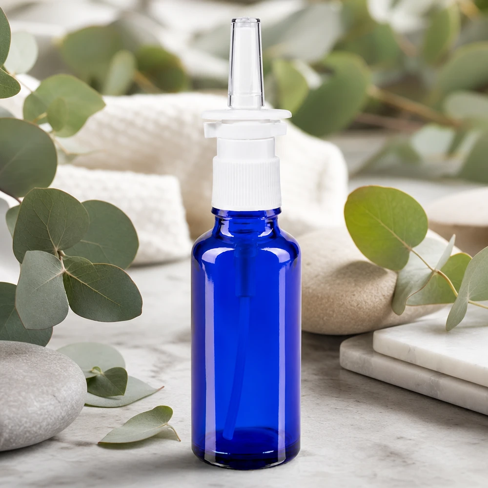 Flacon de pharmacie bleu 30ml vaporisateur nasal blanc Petite bouteille en verre bleue de 30 ml avec applicateur nasal, posée sur du marbre blanc parmi des pierres de bien-être