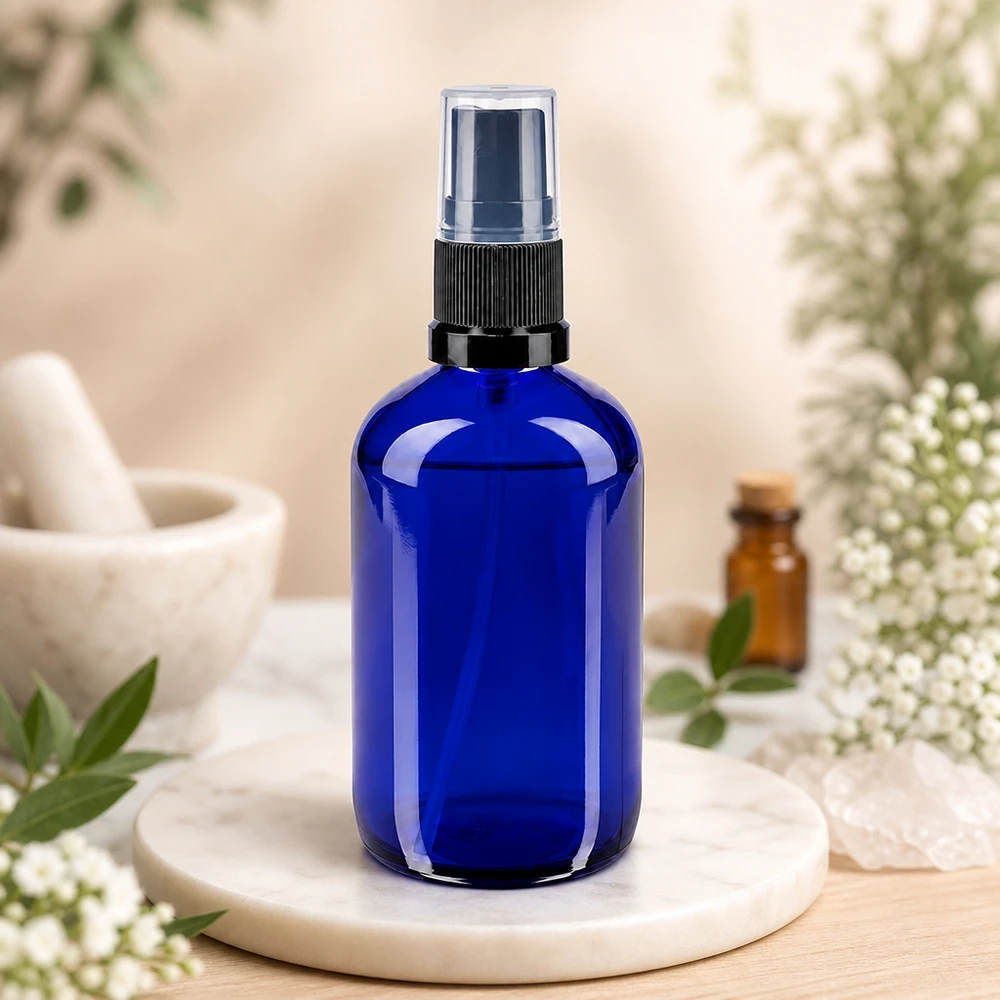 Flacon vaporisateur en verre bleu cobalt de 100 ml, muni d'un bouchon de protection transparent et orné de fleurs blanches