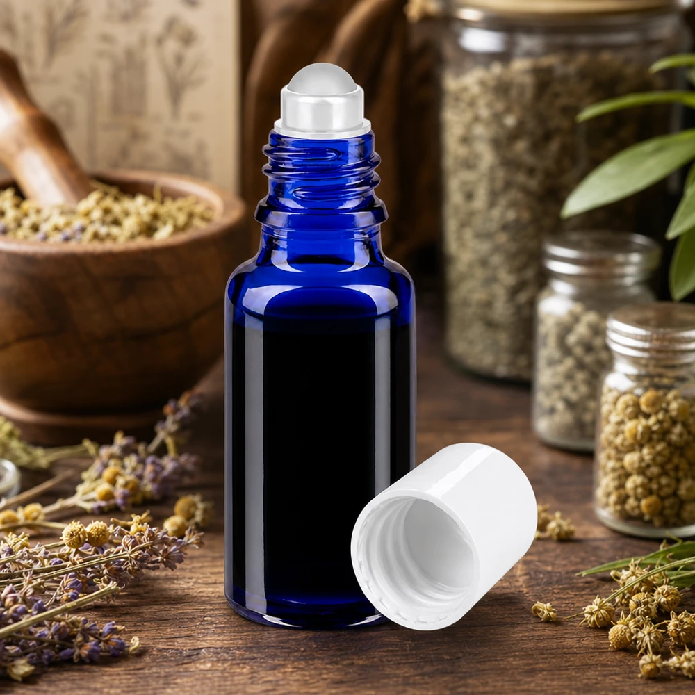 Flacon en verre bleu cobalt de 20 ml à bille, ouvert, posé à côté de bocaux contenant des herbes et des fleurs séchées