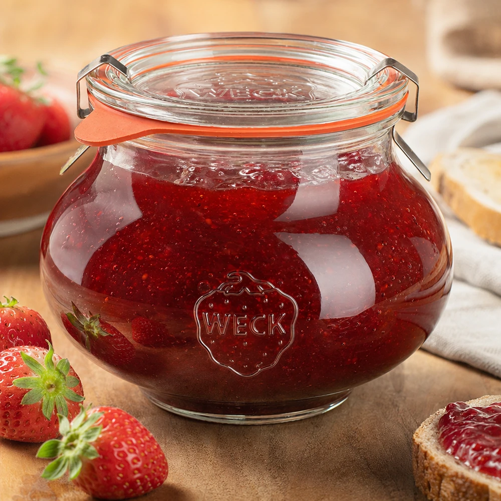 WECK Pot à bijoux 560ml rempli de confiture de fraises maison, fermeture à étrier fermée, entouré d'œufs frais.