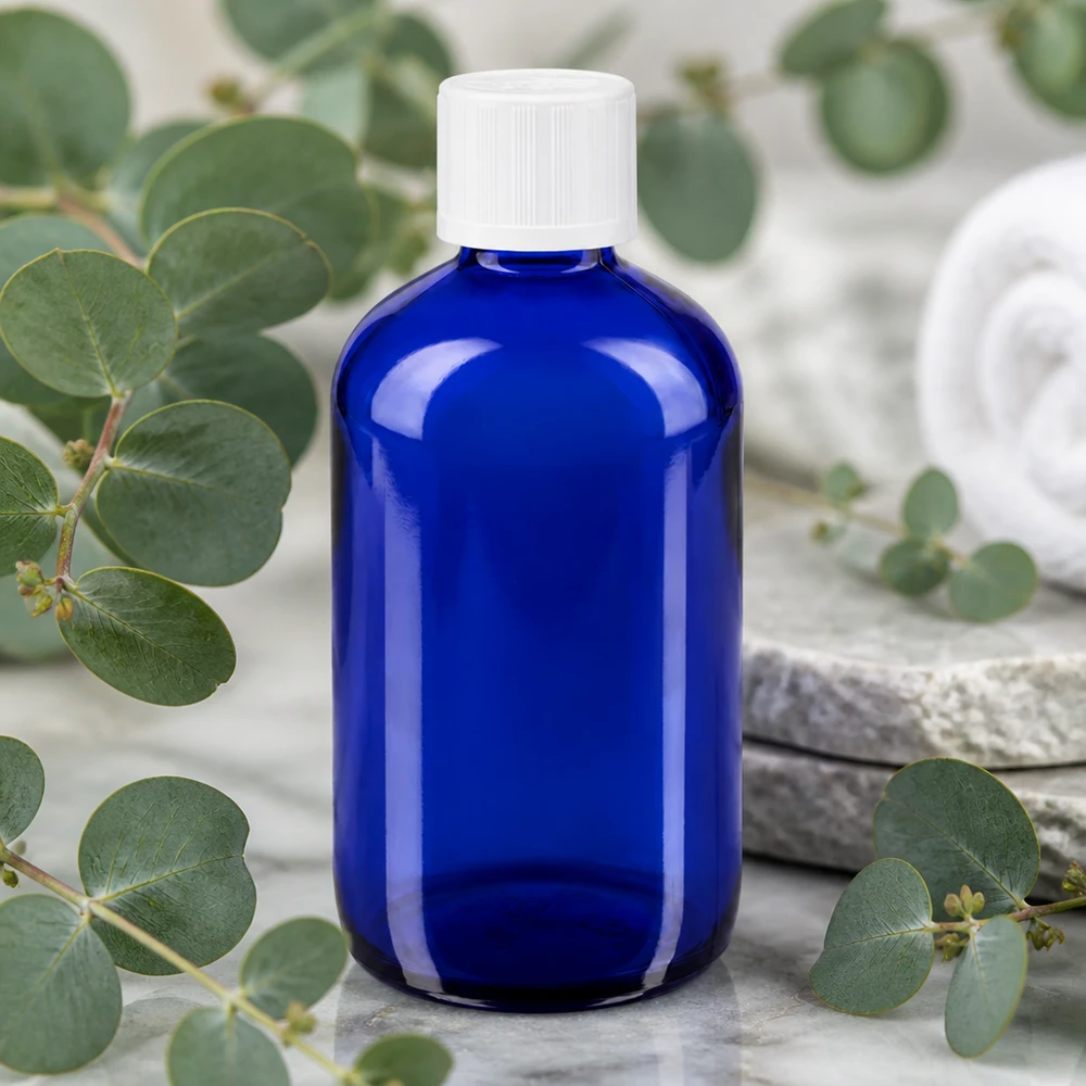 Flacon de pharmacie bleu 100ml bouchon compte-gouttes blanc sécurité enfant std Flacon en verre bleu cobalt de 100 ml avec un bouchon blanc à sécurité enfant, posé sur du marbre et entouré d'herbes naturelles