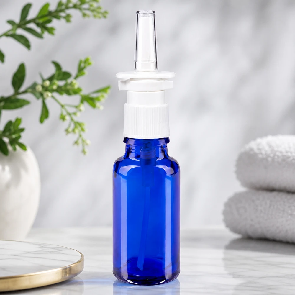 Flacon à pharmacie bleu 20ml vaporisateur nasal blanc standard Flacon compact de spray nasal de 20 ml en verre bleu cobalt, muni d'un embout pulvérisateur blanc, sur fond de paysage naturel