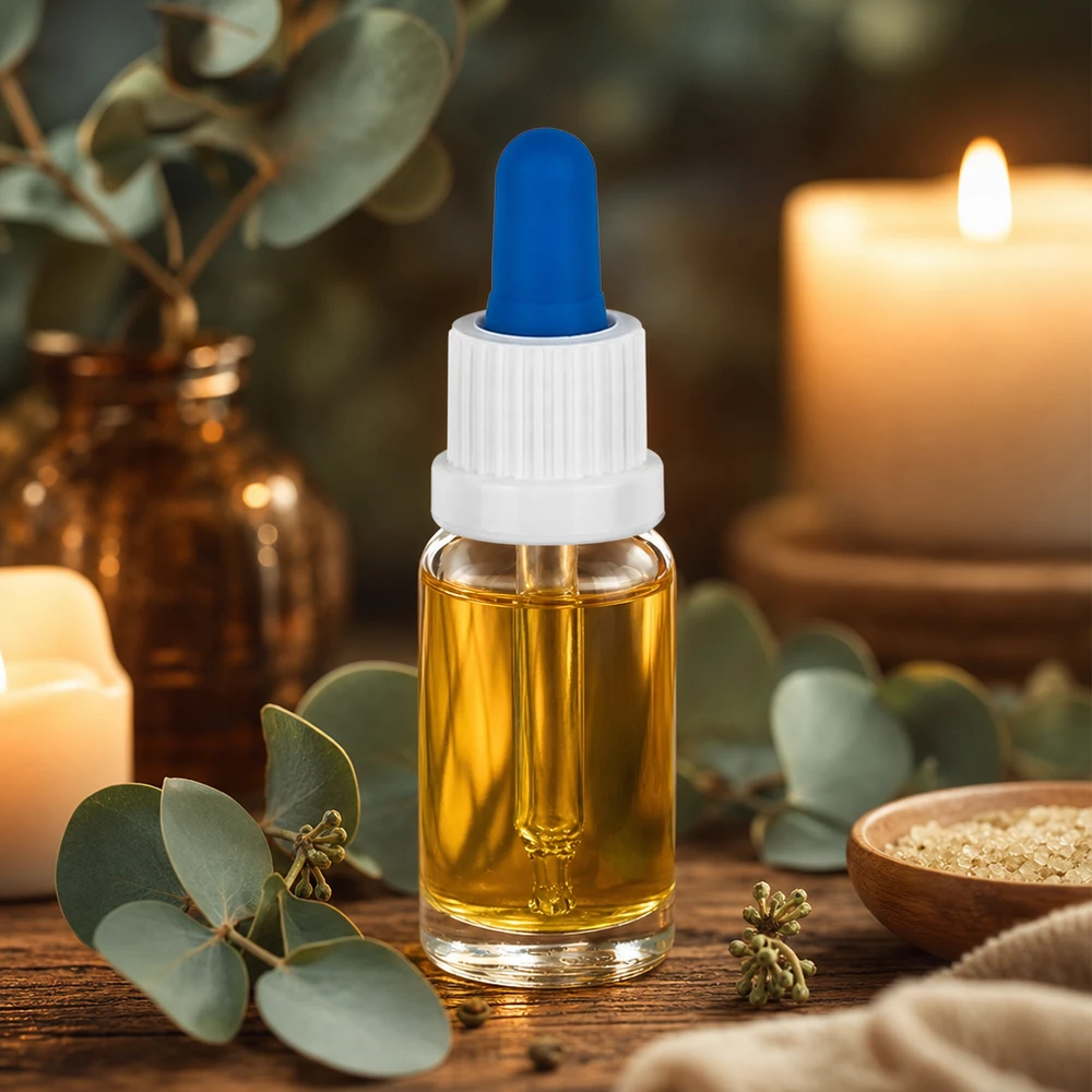 Petit flacon pipette de 10 ml contenant de l'huile dorée, muni d'un bouchon blanc et d'une bille en caoutchouc bleue, posé sur une table en bois