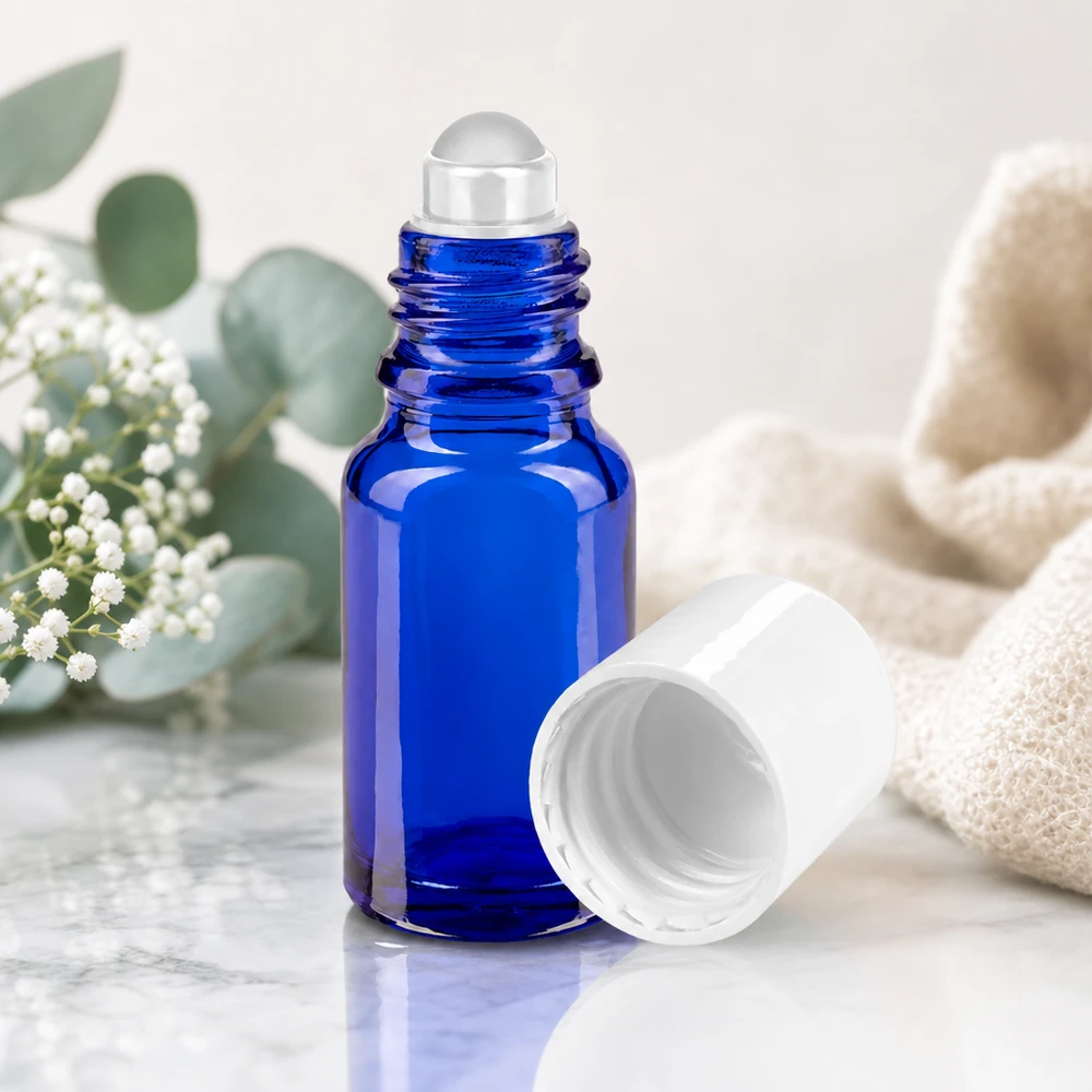 Flacon roll-on de 10 ml en verre de protection bleu avec un bouchon blanc, à côté de branches d'eucalyptus
