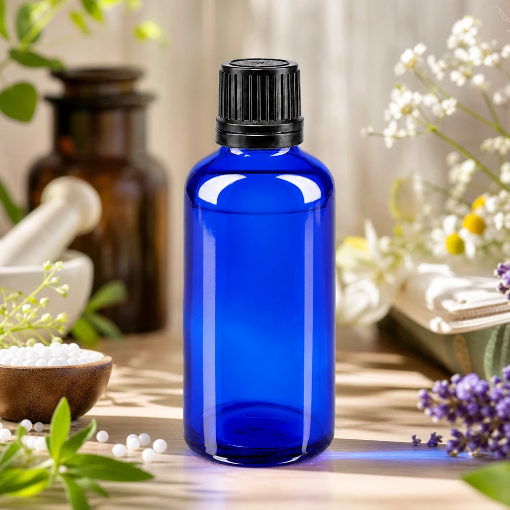 Flacon en verre bleu cobalt de 50 ml avec un OV noir de 8 mm, à côté d'un mortier et de granules homéopathiques