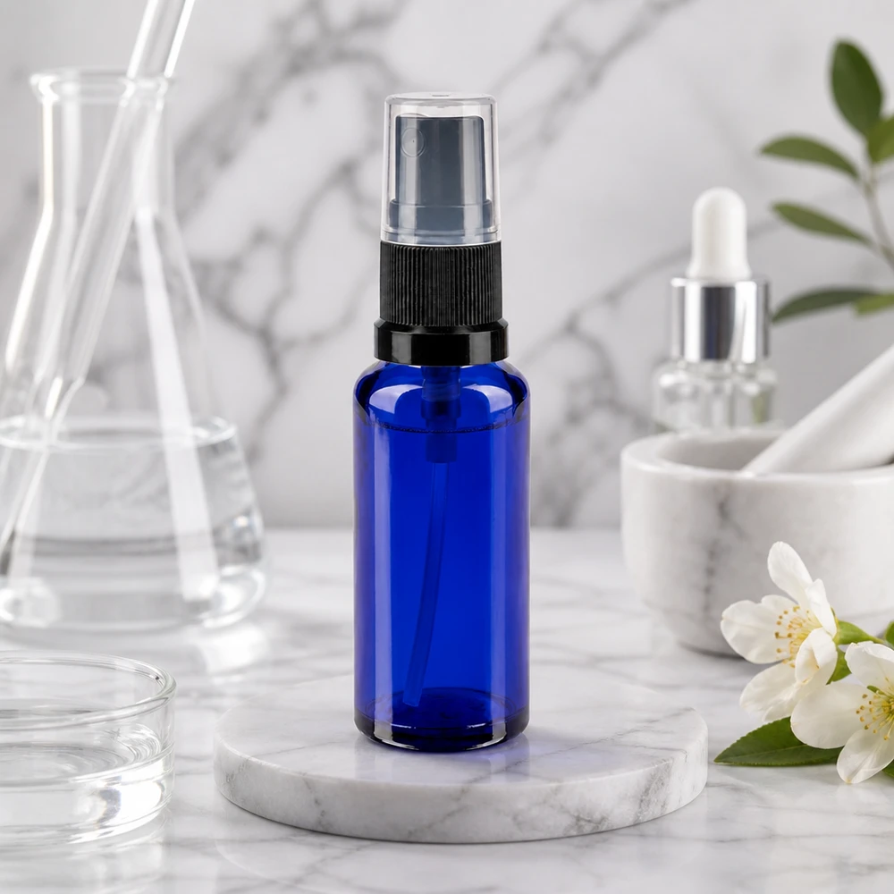Flacon en verre bleu de 30 ml muni d'un vaporisateur fin, noir transparent, à côté de fleurs de jasmin blanches