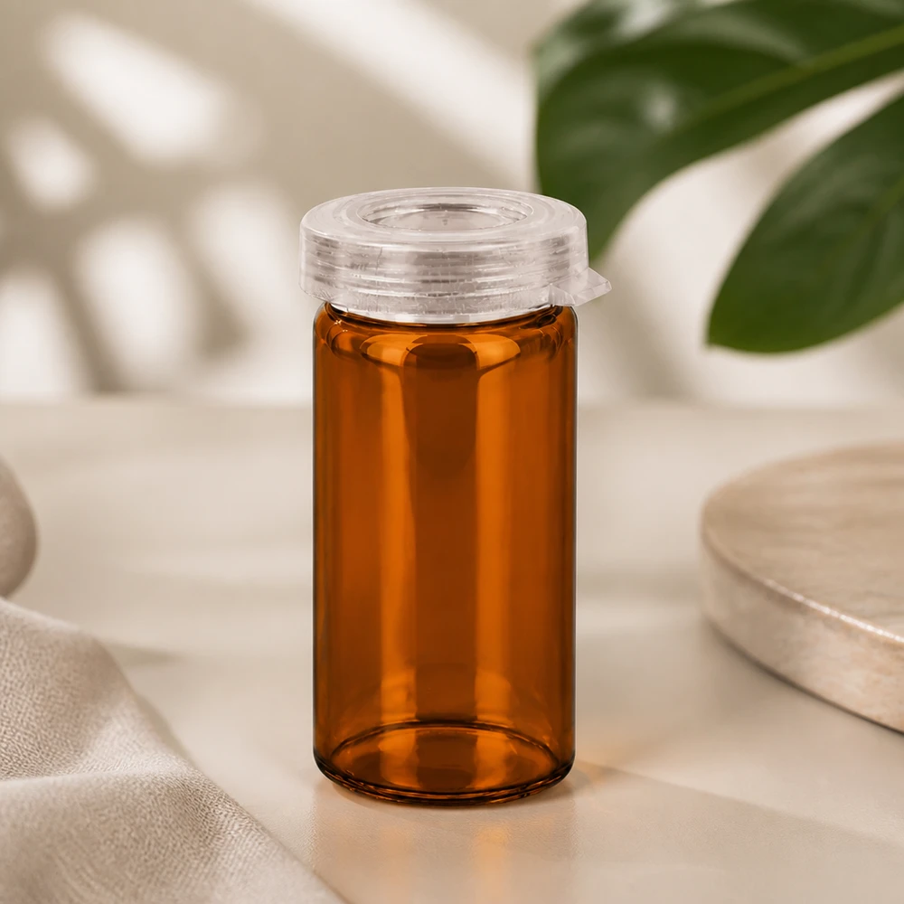 Pot à comprimés 5 ml en verre clair, avec bouchon à déclic Petit flacon de pharmacie de 5 ml en verre ambré, muni d'un bouchon à cliquet de sécurité enfant, à côté d'une feuille de monstera